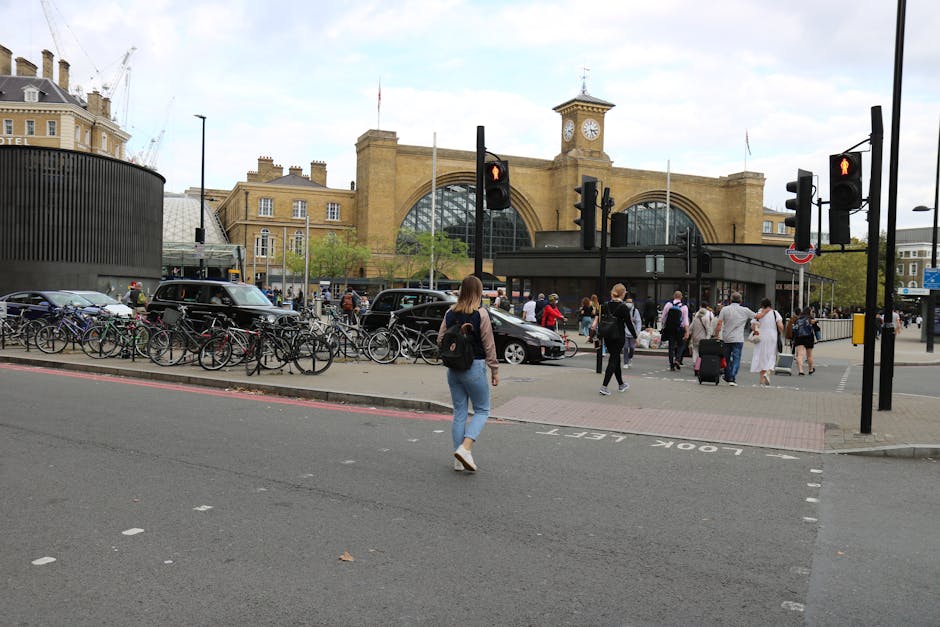 Exterior view of King's Cross railway station in daytime, showing its large brick facade with arched windows and a central clock tower displaying the time. The station is bustling with pedestrians on